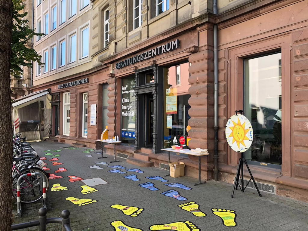 Das Beratungszentrum der KEK von außen mit einem Glücksrad und Fußabdrücken, mit denen man seinen ökologischen Fußabdruck bestimmen kann. 